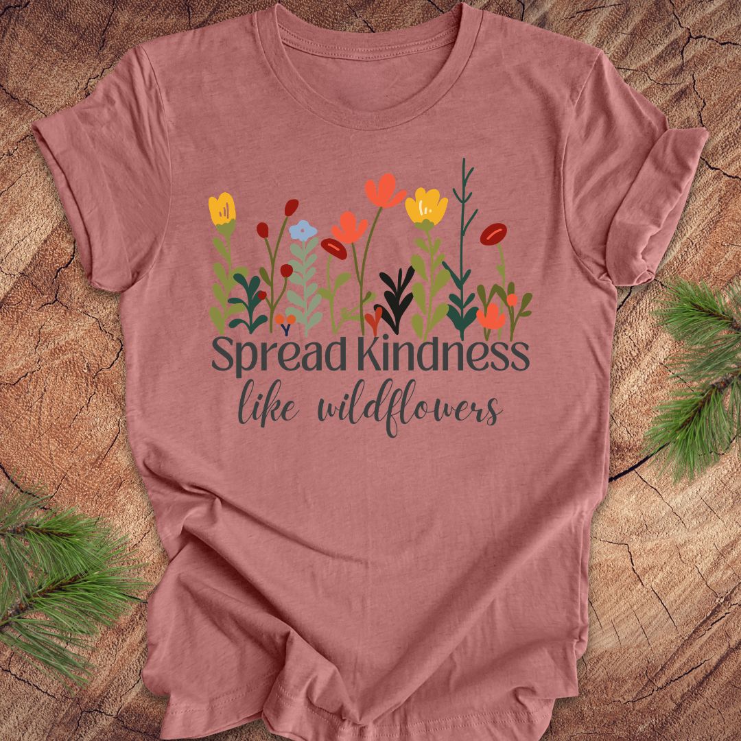 Mauve t-shirt with floral design and 'Spread kindness like wildflowers' text on a wooden surface.