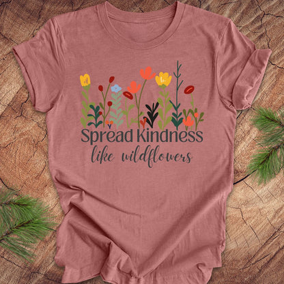 Mauve t-shirt with floral design and 'Spread kindness like wildflowers' text on a wooden surface.