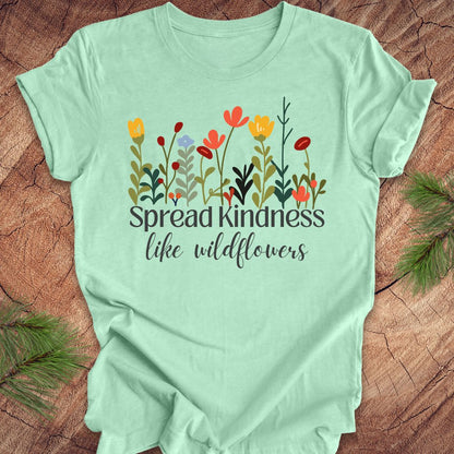 Mint green t-shirt with floral design and 'Spread kindness like wildflowers' text on a wooden surface.