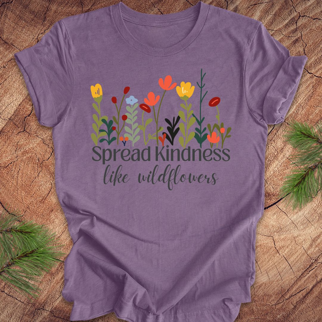 Purple t-shirt with floral design and 'Spread kindness like wildflowers' text on a wooden surface.