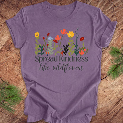 Purple t-shirt with floral design and 'Spread kindness like wildflowers' text on a wooden surface.