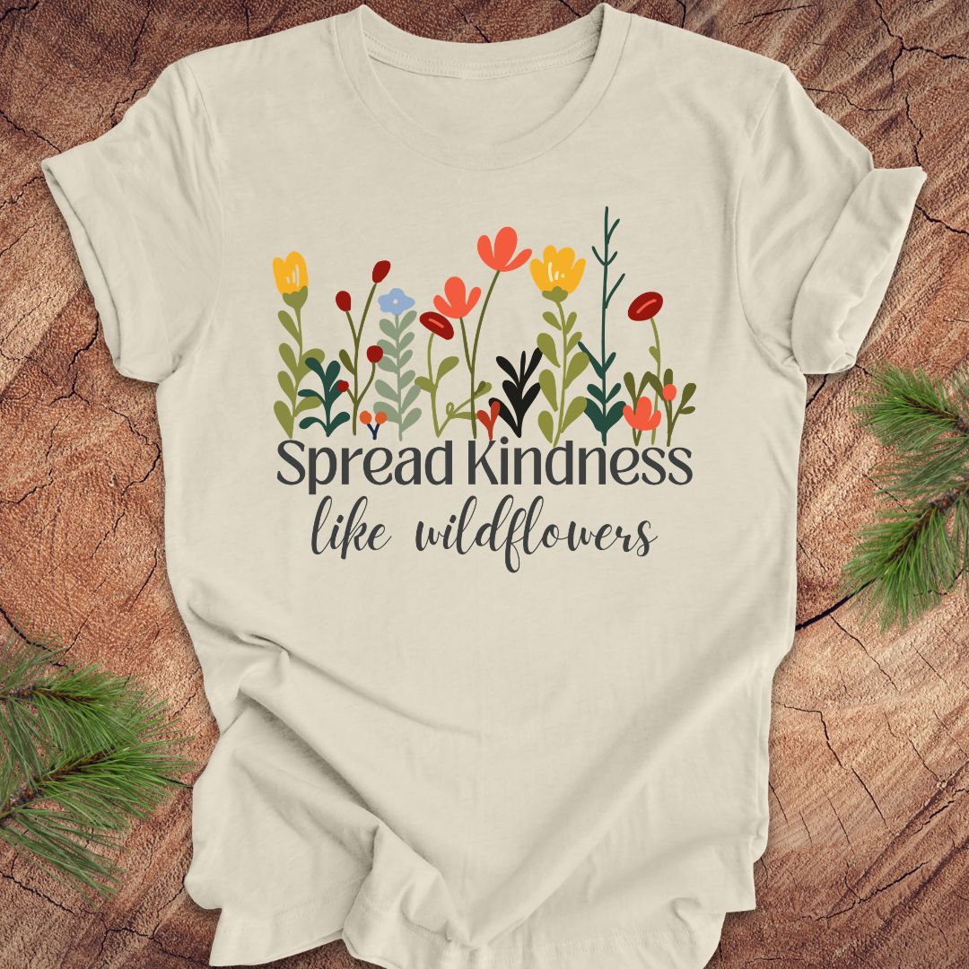 Beige t-shirt with floral design and 'Spread kindness like wildflowers' text on a wooden surface.