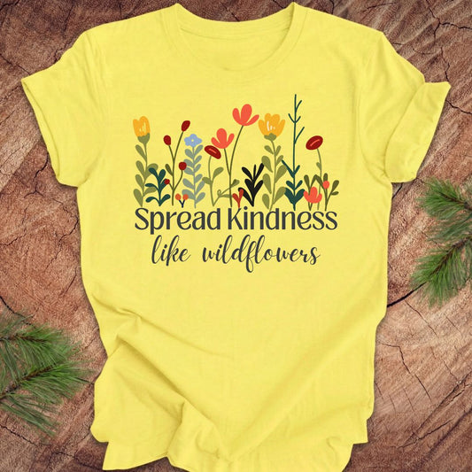 Yellow t-shirt with floral design and 'Spread Kindness like wildflowers' text on a wooden surface.