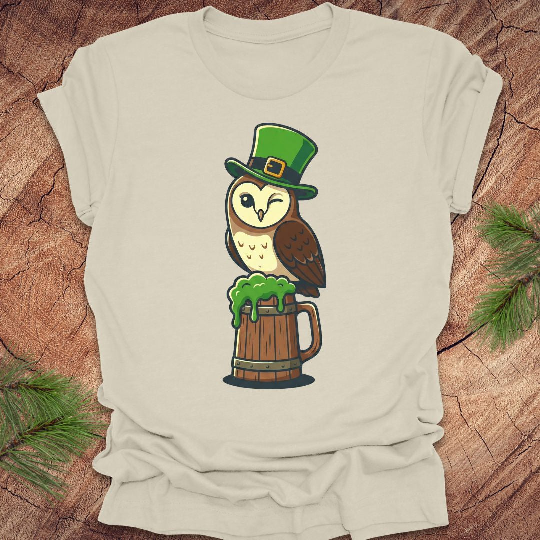 Beige t-shirt with an owl design wearing a green hat and holding a beer mug on a wooden surface.