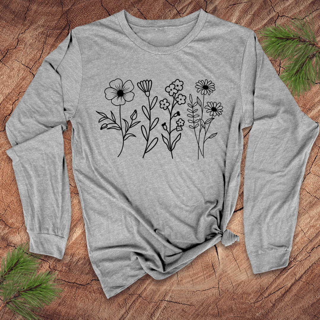 gray long sleeve tshirt with white individual flowers on a wooden surface with pine needles