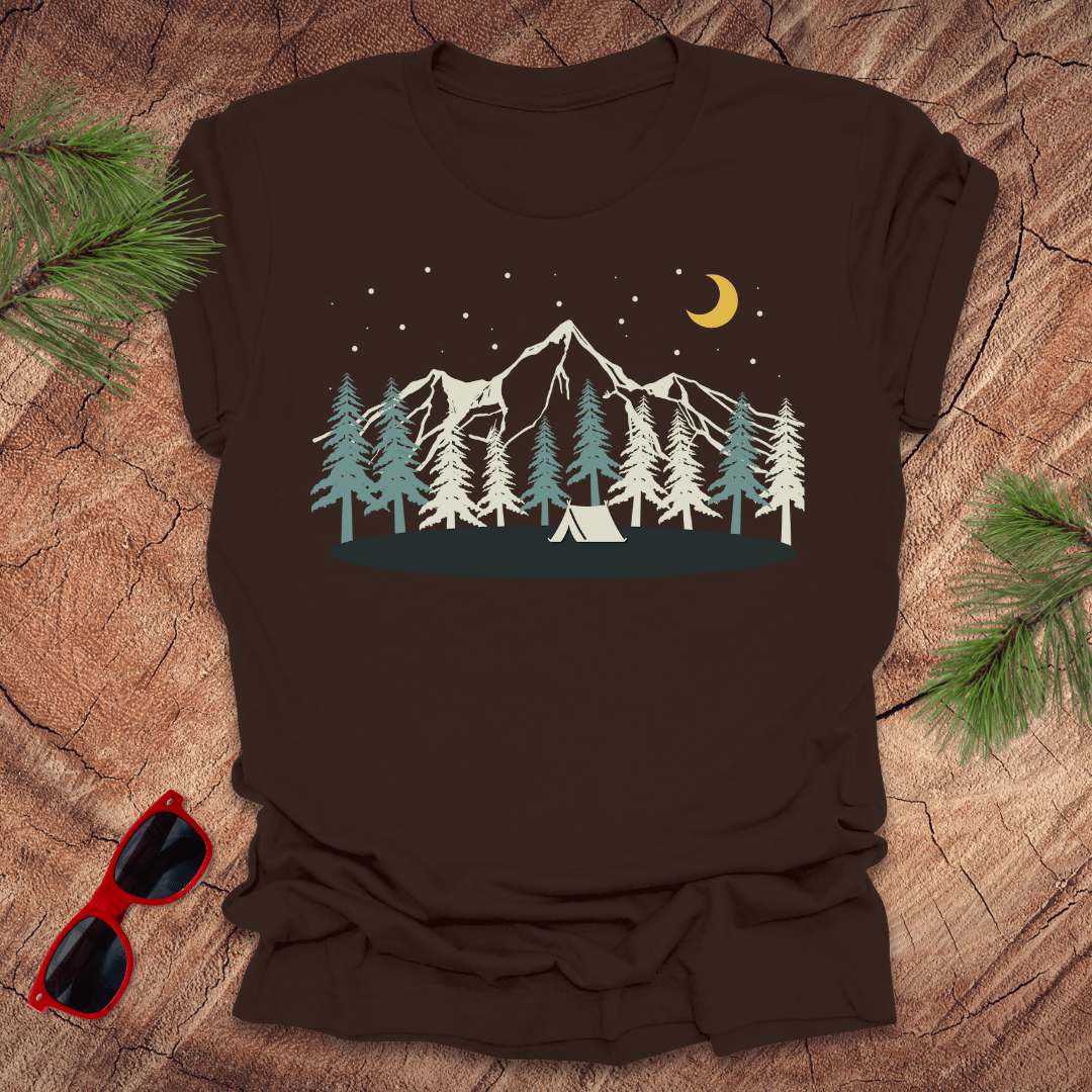 Brown t-shirt with mountain and tent design on a wooden surface with sunglasses and pine branches.