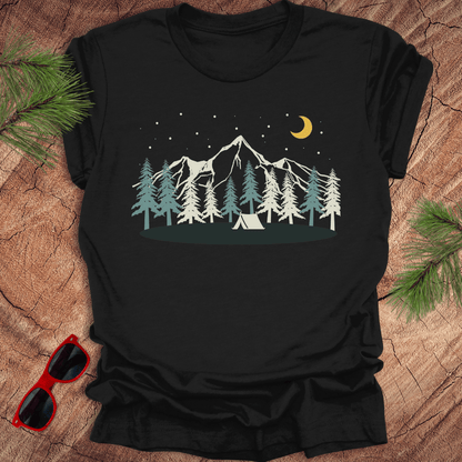 Black t-shirt with mountain and tent design on a wooden surface with sunglasses and pine branches.