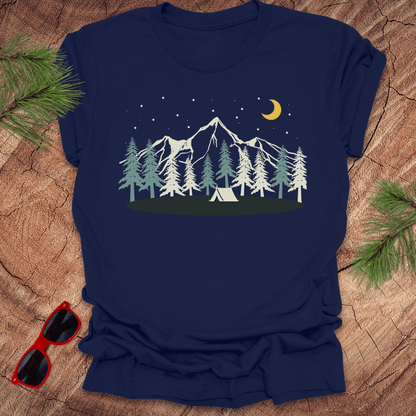 Navy blue t-shirt with a mountain and tent design on a wooden surface with sunglasses and pine branches.