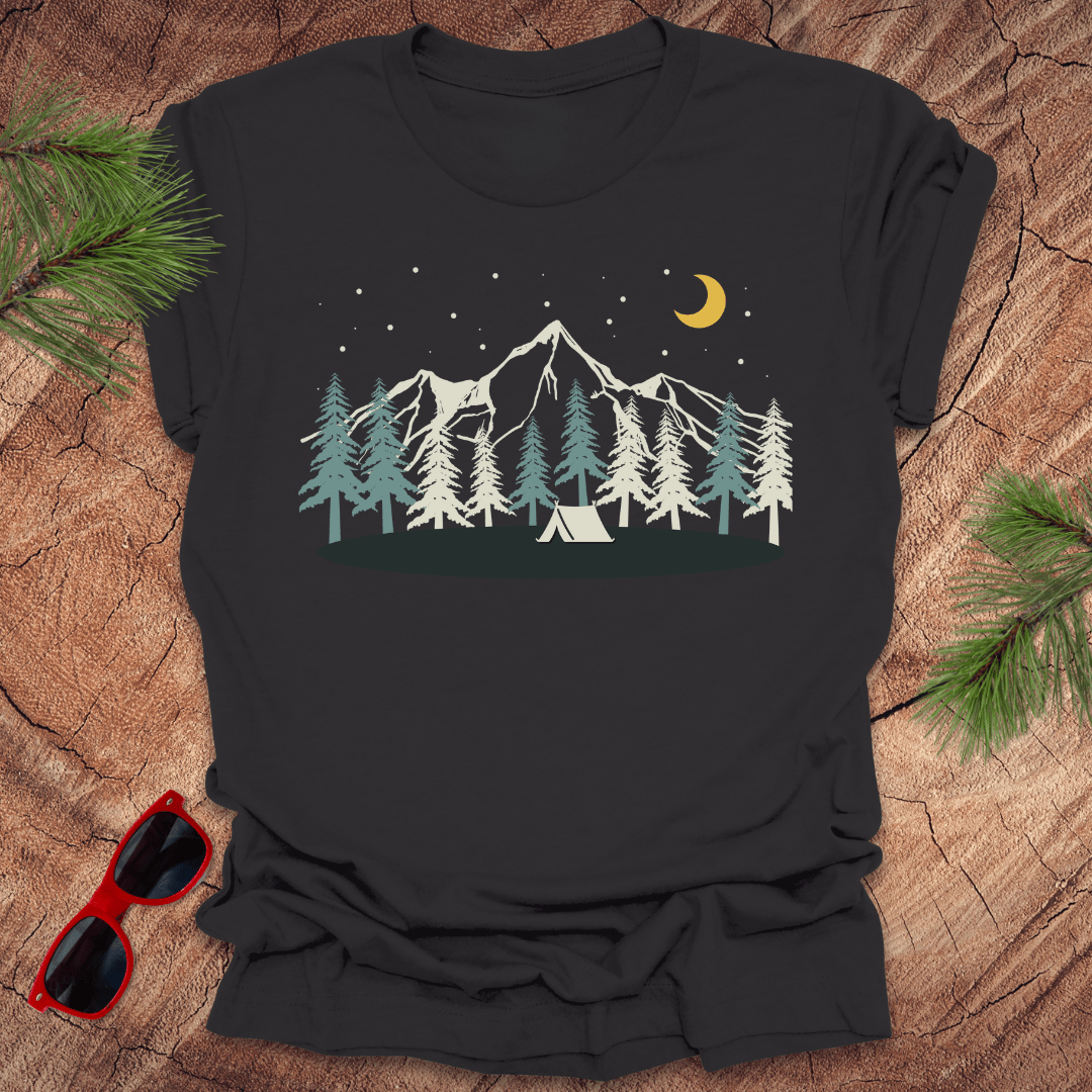 Black t-shirt with mountain and tent design on a wooden surface with sunglasses and pine branches.