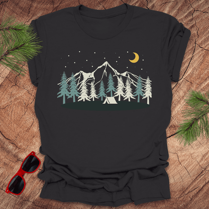 Black t-shirt with mountain and tent design on a wooden surface with sunglasses and pine branches.