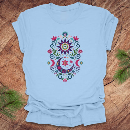 Light blue t-shirt with a colorful moon, stars and flower mandala design on a wooden surface