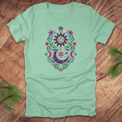 Light green t-shirt with a colorful moon, stars and flower mandala design on a wooden surface