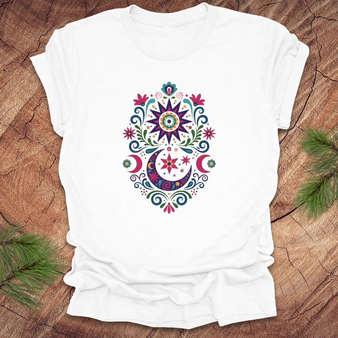 White t-shirt with a colorful moon, stars and flower mandala design on a wooden surface