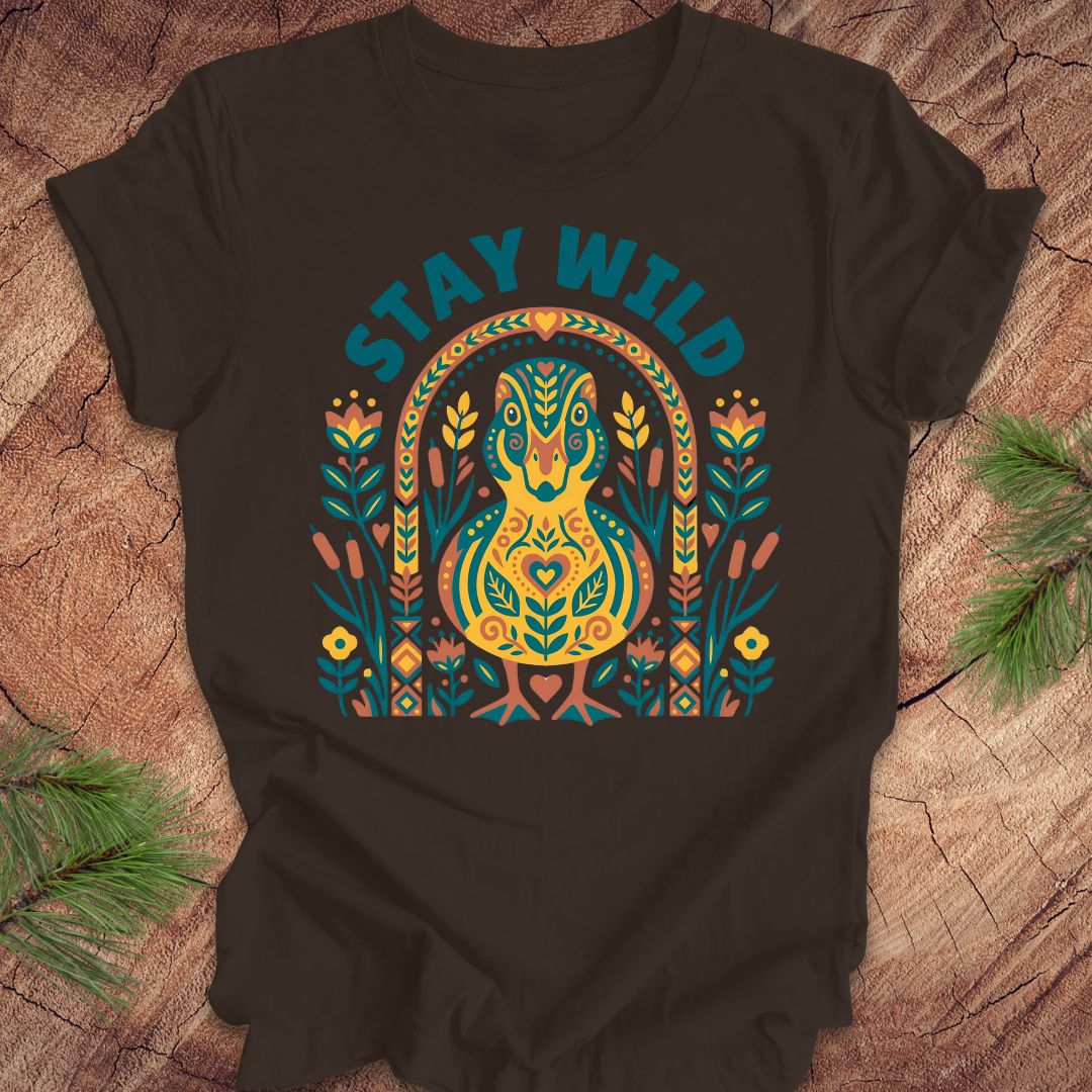 Brown t-shirt with colorful duck graphic and 'Stay Wild' text on a wooden surface.
