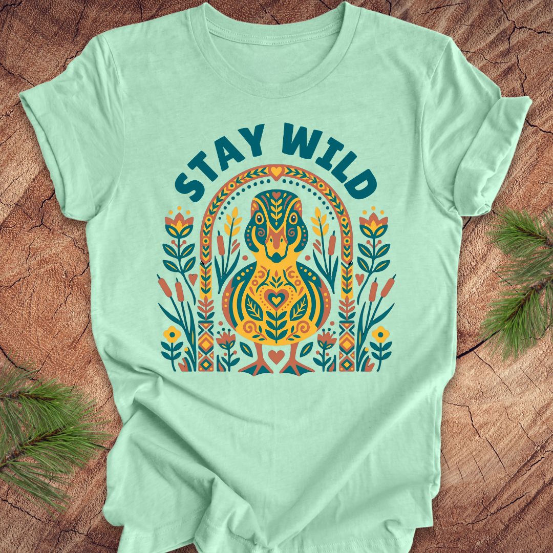 Mint green t-shirt with colorful duck graphic and 'Stay Wild' text on a wooden surface.