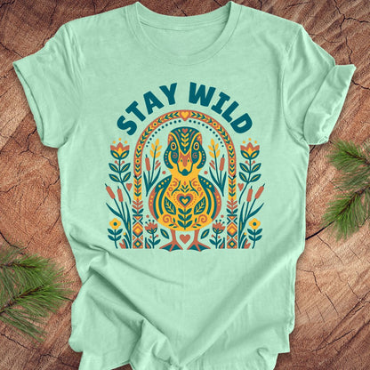 Mint green t-shirt with colorful duck graphic and 'Stay Wild' text on a wooden surface.