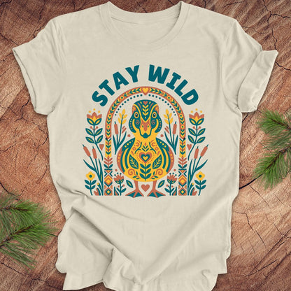 Beige t-shirt with colorful duck graphic and 'Stay Wild' text on a wooden surface.