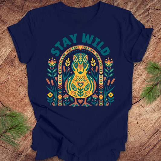 Navy blue t-shirt with colorful duck graphic and 'Stay Wild' text on a wooden surface.