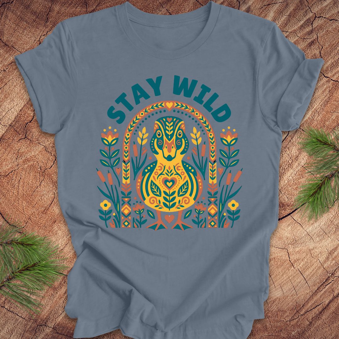 Blue t-shirt with colorful duck graphic and 'Stay Wild' text on a wooden surface.