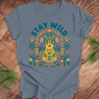 Blue t-shirt with colorful duck graphic and 'Stay Wild' text on a wooden surface.