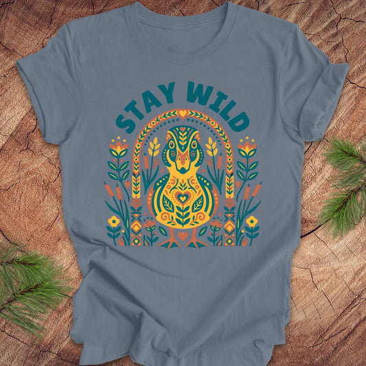 Blue t-shirt with colorful duck graphic and 'Stay Wild' text on a wooden surface.