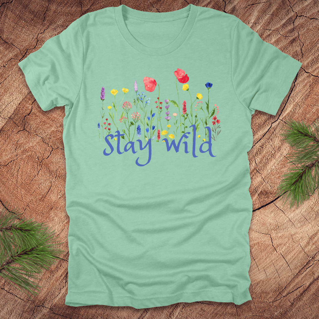 Mint green tshirt with the text, 'stay wild' with wildflowers on a wooden background.