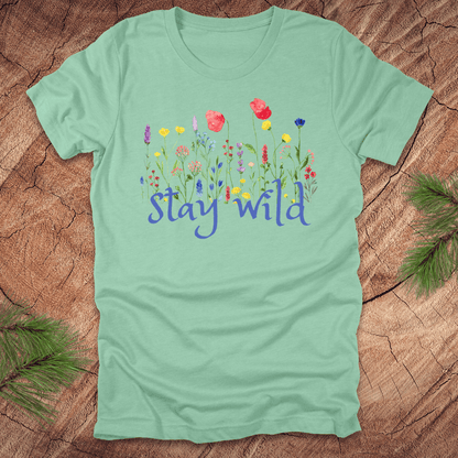 Mint green tshirt with the text, 'stay wild' with wildflowers on a wooden background.