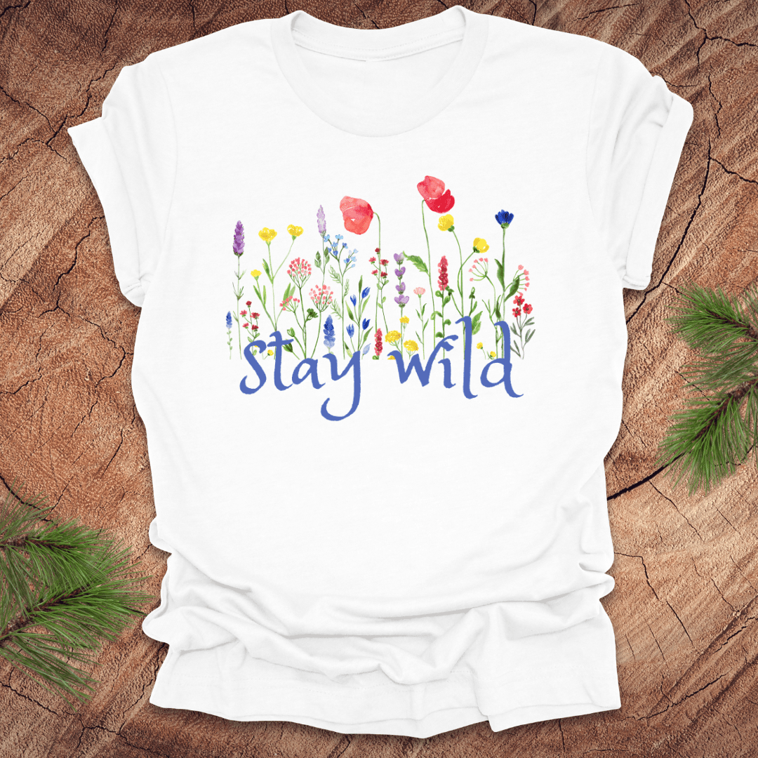 White tshirt with the text, 'stay wild' with wildflowers on a wooden background.