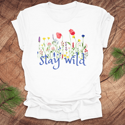 White tshirt with the text, 'stay wild' with wildflowers on a wooden background.