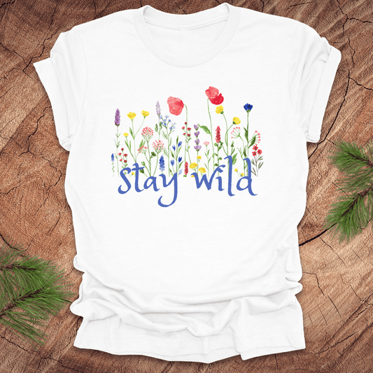 White tshirt with the text, 'stay wild' with wildflowers on a wooden background.
