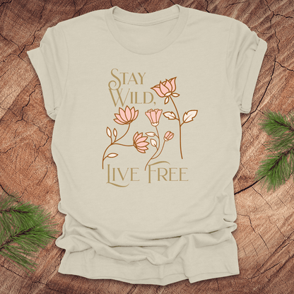 Beige t-shirt with 'Stay Wild, Live Free' text and floral design on a wooden surface.