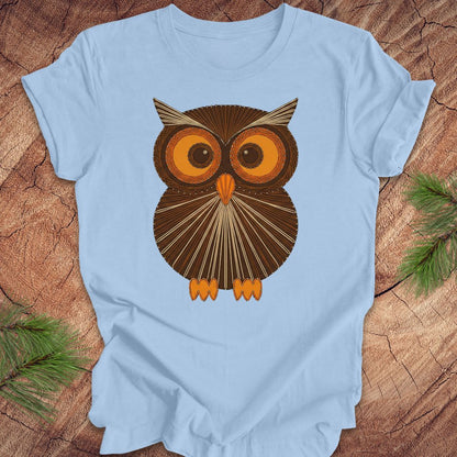 Light blue colored t-shirt with a vintage owl design on a wooden surface