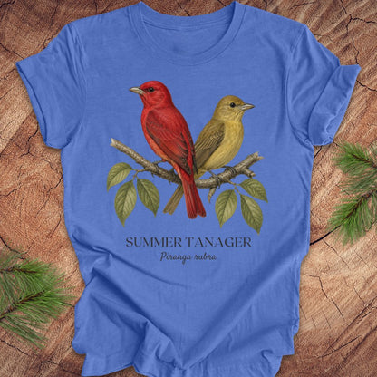 Blue t-shirt with male and female summer tanager bird illustration on a wooden surface