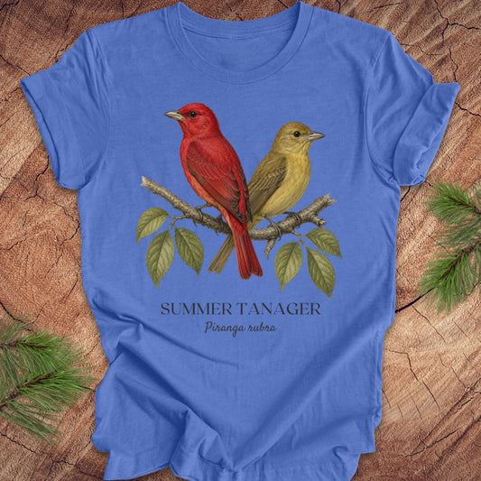 Blue t-shirt with male and female summer tanager bird illustration on a wooden surface