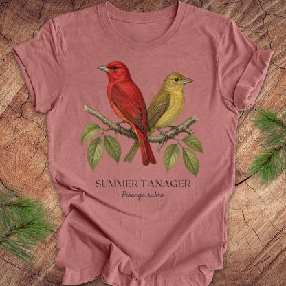 Mauve t-shirt with male and female summer tanager bird illustration on a wooden surface