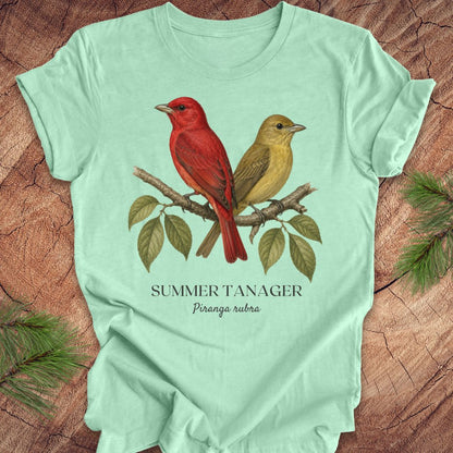 Mint green t-shirt with male and female summer tanager bird illustration on a wooden surface