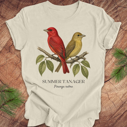 Beige t-shirt with male and female summer tanager bird illustration on a wooden surface