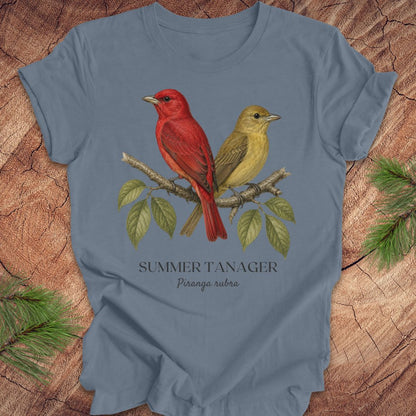 Blue t-shirt with male and female summer tanager bird illustration on a wooden surface