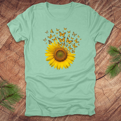 Light green t-shirt with a sunflower and butterfly design on a wooden surface.