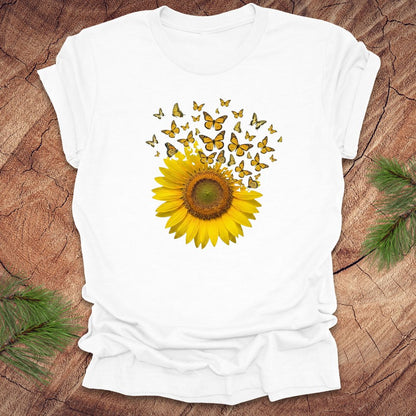 White t-shirt with a sunflower and butterflies design on a wooden surface.