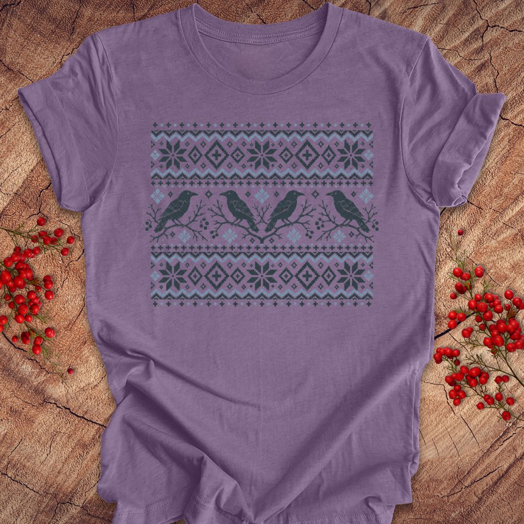 A lavender purple short-sleeve t-shirt with a winter-themed graphic print featuring three birds and snowflake patterns, laid flat on a rustic wood background with red berries.