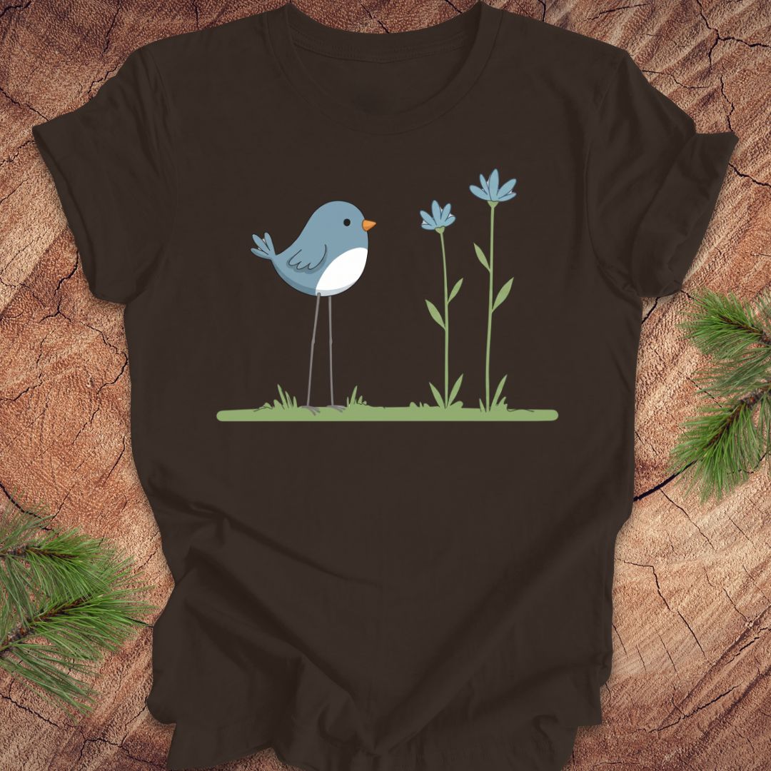 Brown t-shirt with a blue bird and flowers design on a wooden surface.