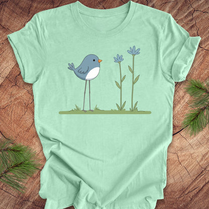 Mint green t-shirt with a blue bird and flowers design on a wooden surface.