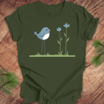 Green t-shirt with a blue bird and flowers design on a wooden surface.