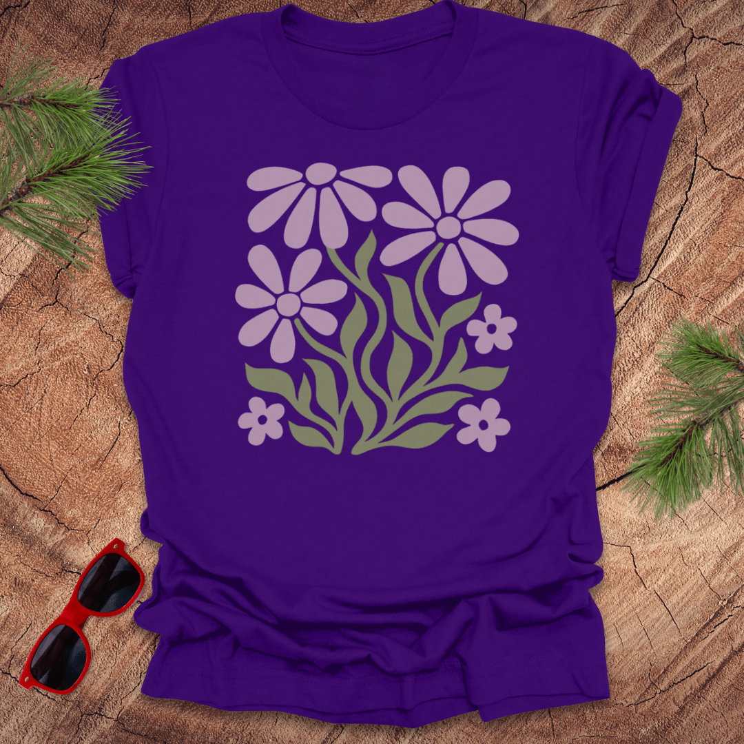 Purple t-shirt with floral design on a wooden surface with sunglasses and greenery.