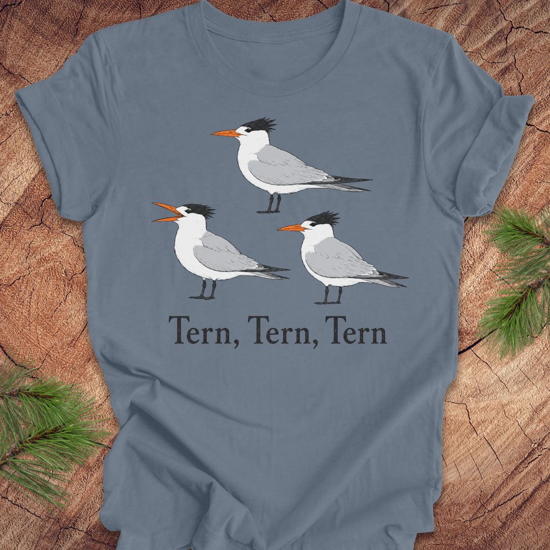 A slate blue t-shirt with three tern birds and text, 'tern, tern, tern' on a wood background. 