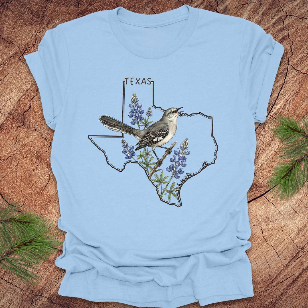 Baby blue t-shirt with Texas state outline with state bird, mockingbird and state flower bluebonnet design on a wooden surface