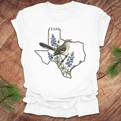 White t-shirt with Texas state outline with state bird, mockingbird and state flower bluebonnet design on a wooden surface