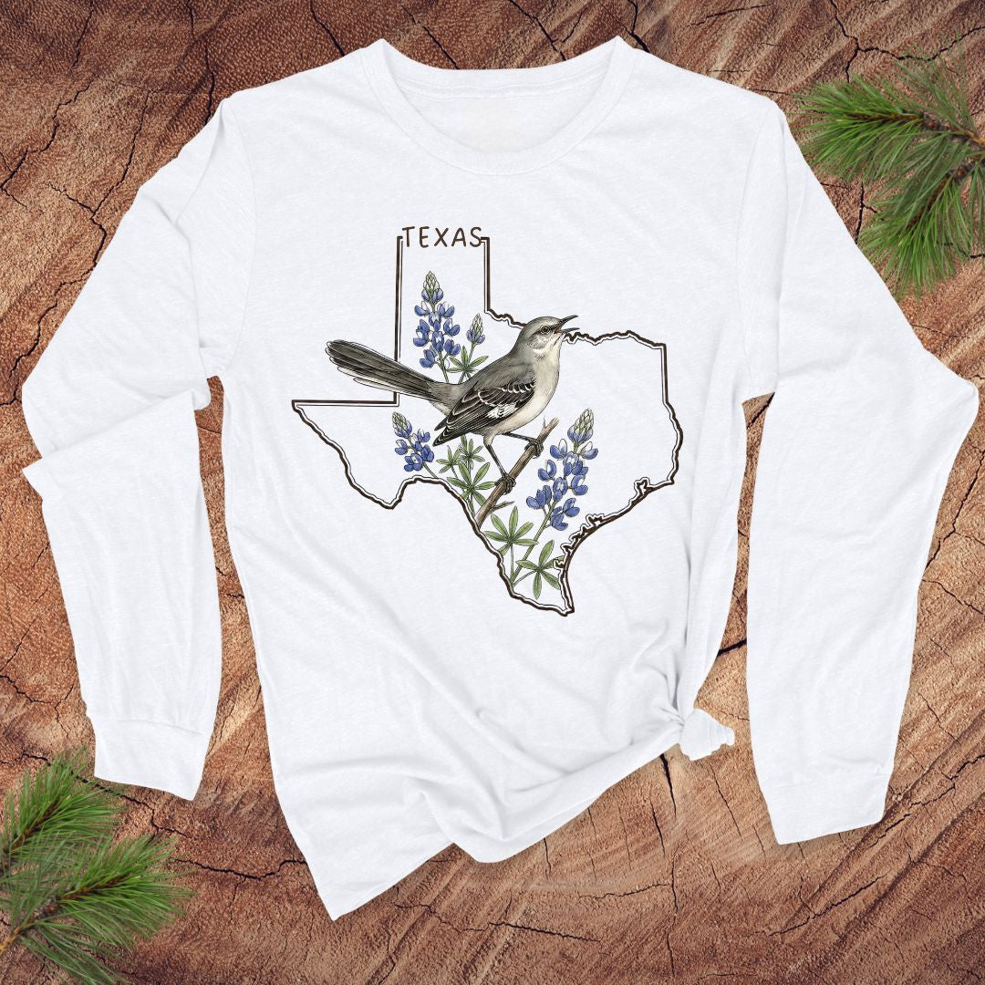 White long-sleeve shirt with Texas design featuring a bird and bluebonnets on a wooden surface.