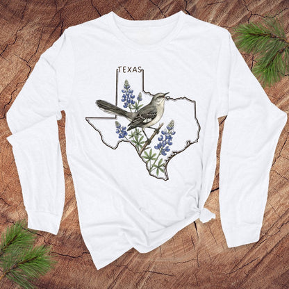 White long-sleeve shirt with Texas design featuring a bird and bluebonnets on a wooden surface.